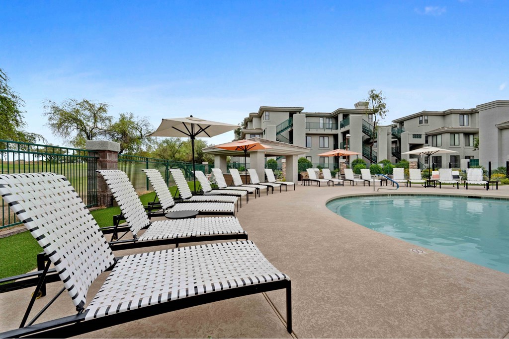 A pool area with sun loungers and a building in the background.