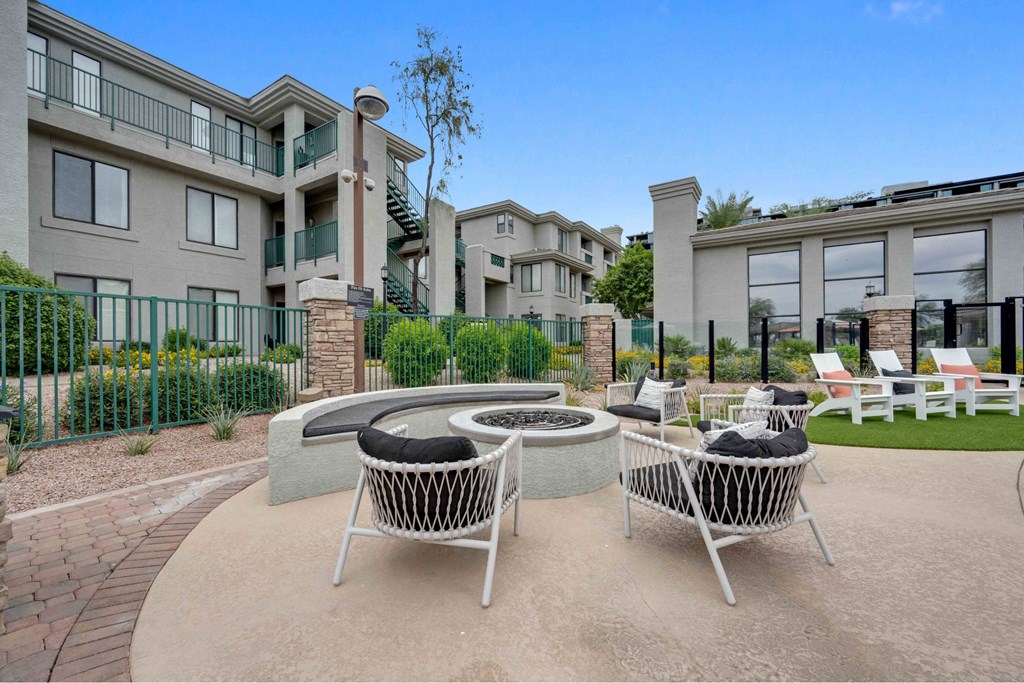 A patio with two chairs and a fire pit in front of apartment buildings.