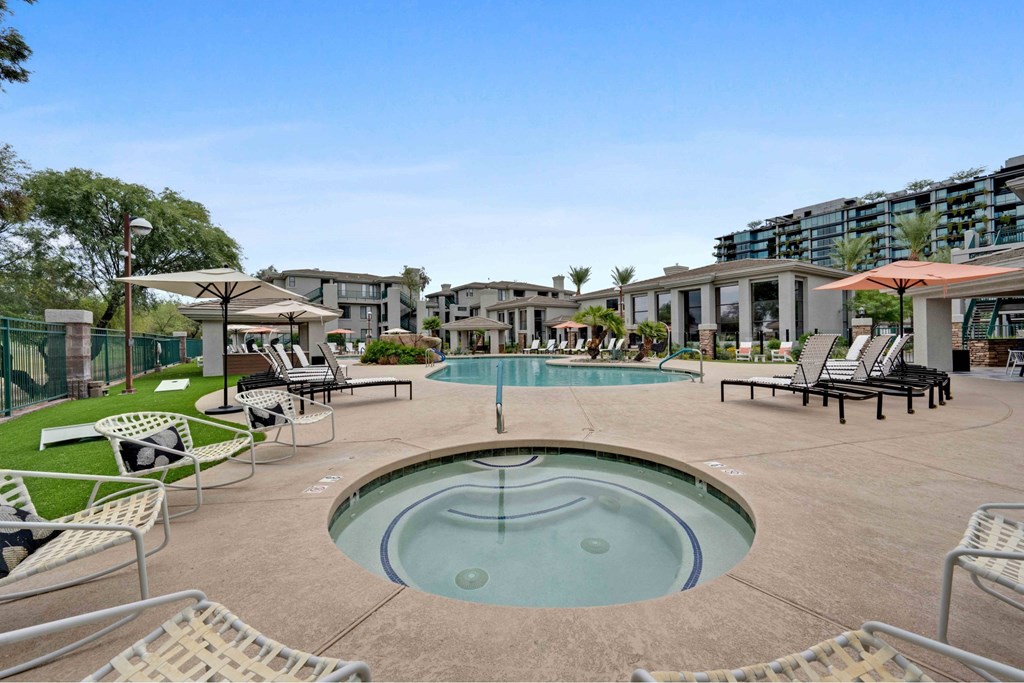 A large outdoor pool with a hot tub and lounge chairs.