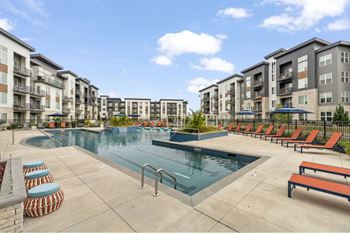 a swimming pool with orange chairs around it in front of an apartment building