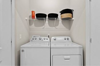 a white washer and dryer in a small laundry room with a shelf above