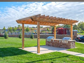 A wooden pergola structure is situated in a grassy area with a mailbox and a fence in the background.