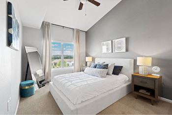 A bedroom with a large bed, a ceiling fan, and a window with curtains.