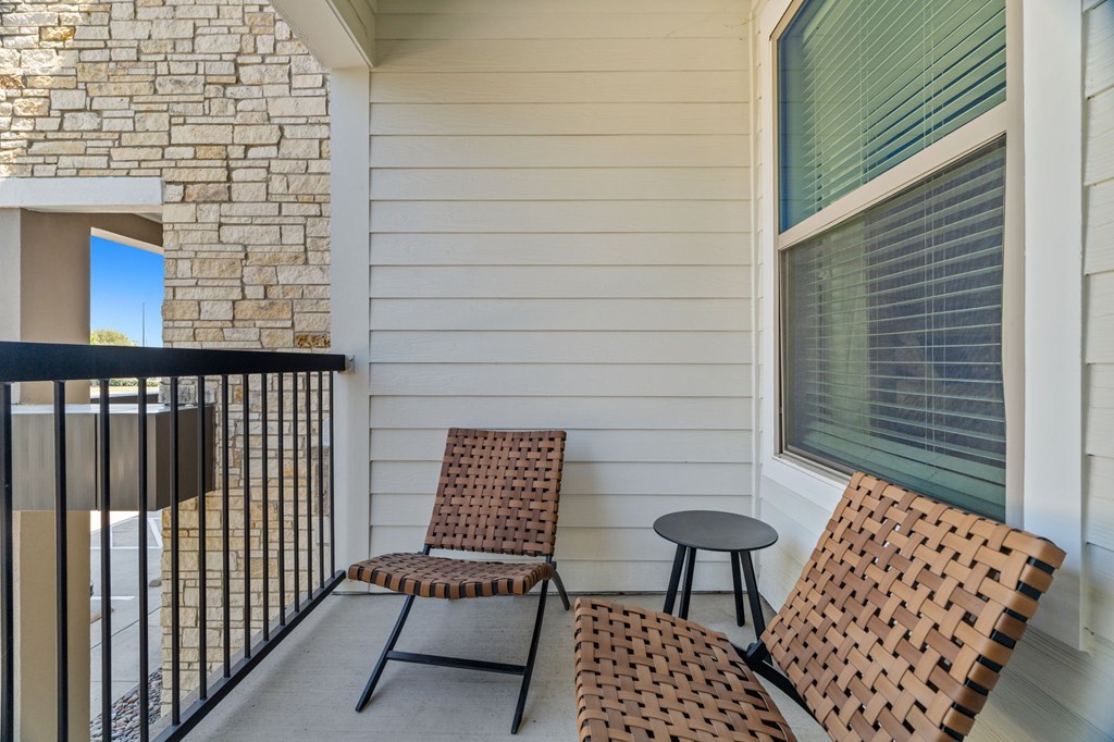 Two chairs and a small table are on a balcony.