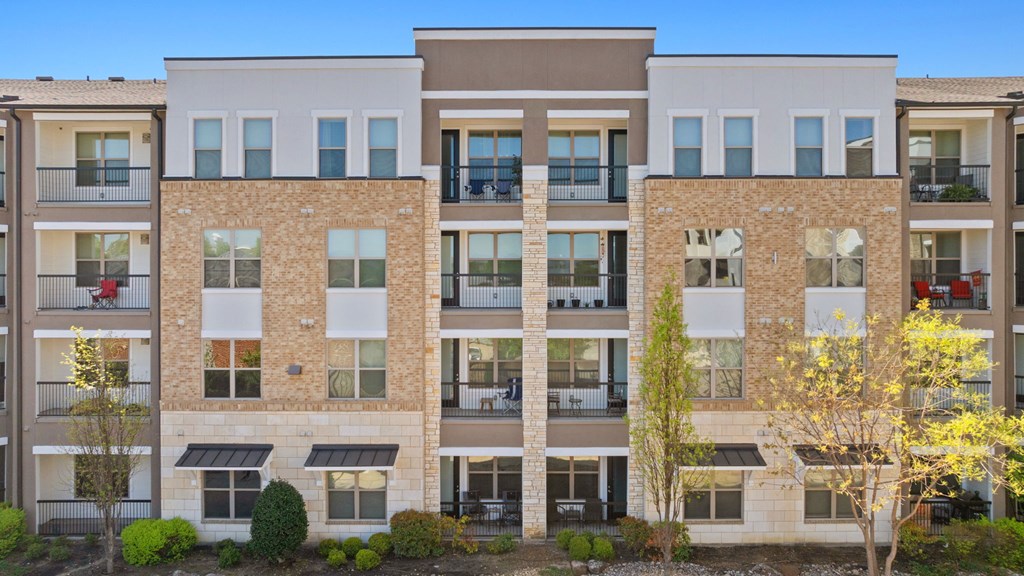 A row of apartment buildings with balconies and trees in front.