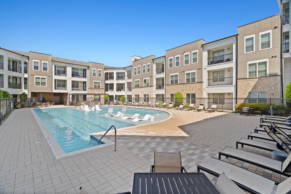 A swimming pool surrounded by apartment buildings and lounge chairs.