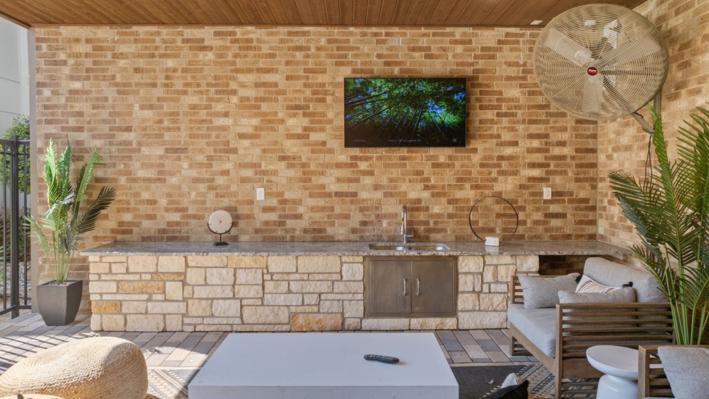 A modern outdoor living space with a brick wall and a television mounted above a fireplace.