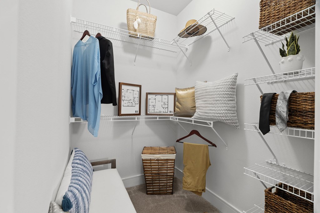 A white closet with clothes and baskets on the shelves.