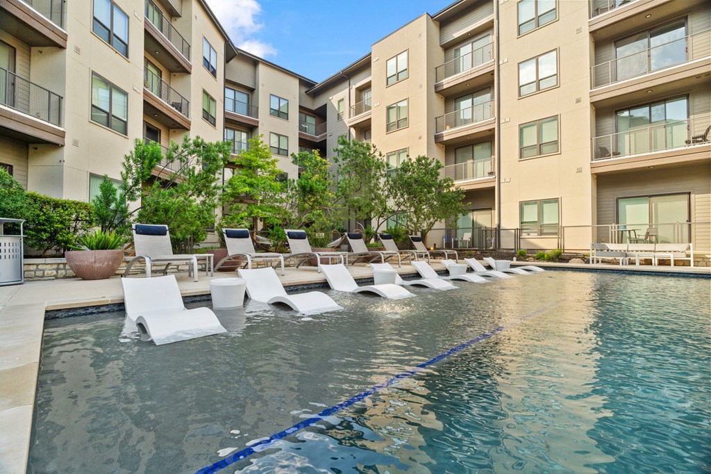 A pool with lounge chairs in front of apartment buildings.