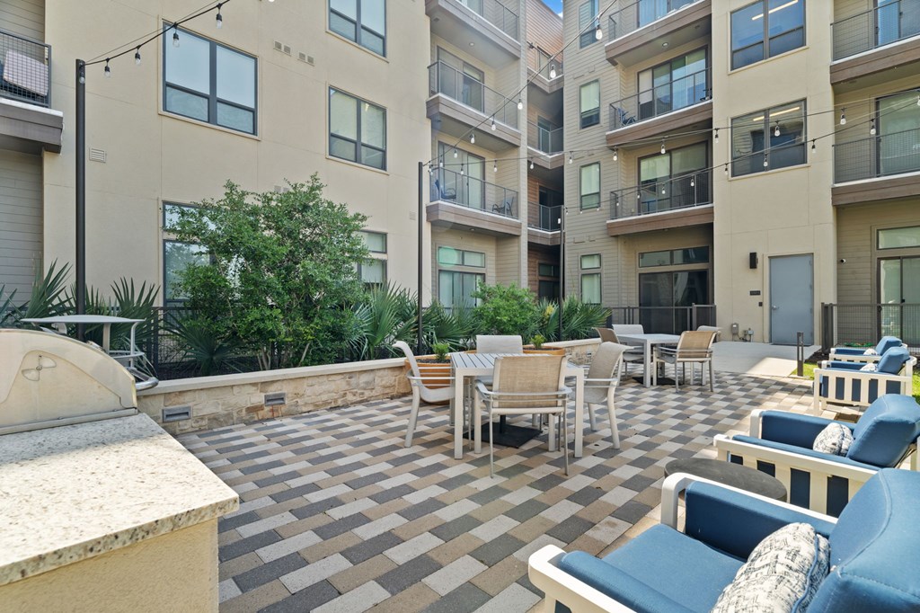 A patio with chairs and tables is surrounded by apartment buildings.