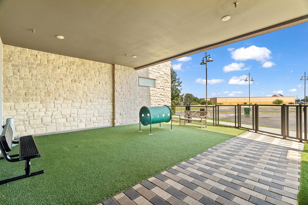 A patio area with a bench, a green trash can, and a brick wall.