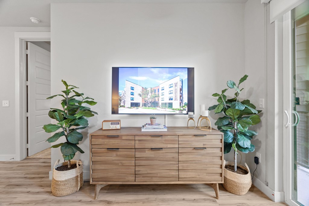A TV is on a wooden cabinet in a room with two potted plants.