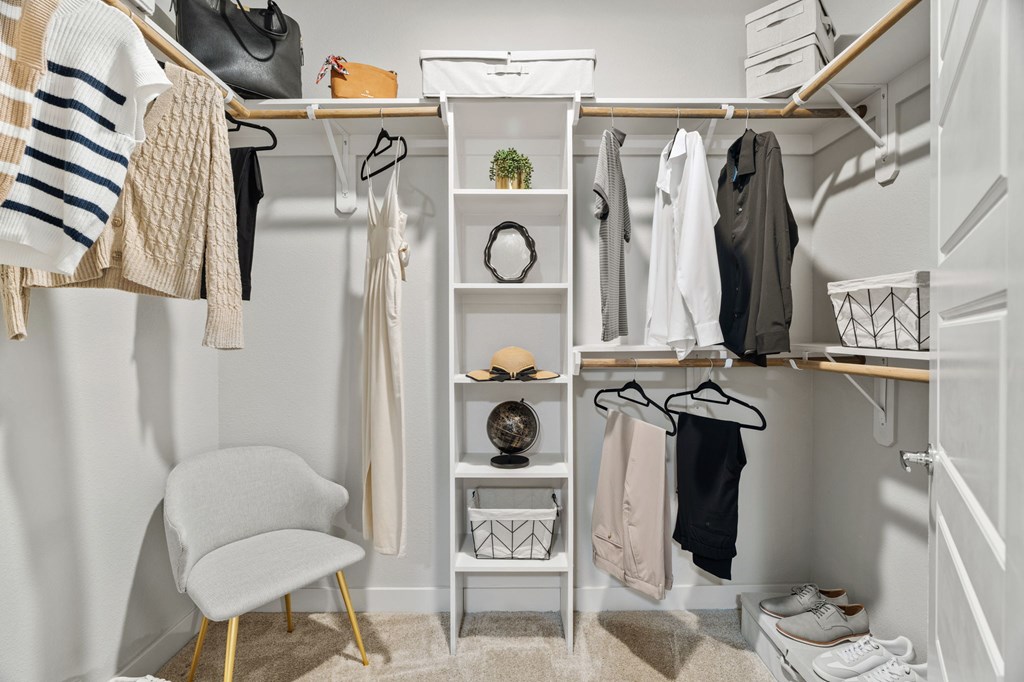A white closet with clothes and a chair.
