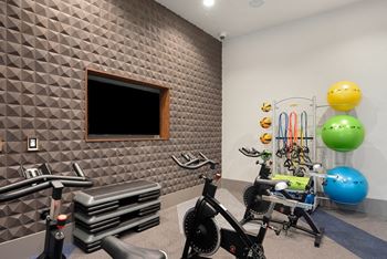 A gym with a variety of equipment including a stationary bike, a rowing machine, and a wall-mounted television.