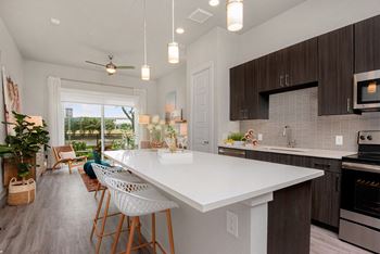 A modern kitchen with a white island and wooden chairs.