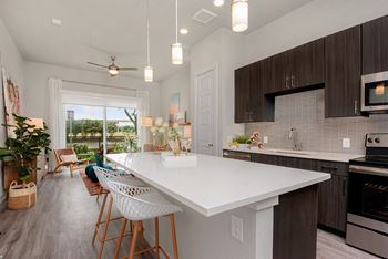 A modern kitchen with a white island and wooden chairs.