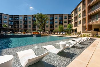 A pool with sun loungers and apartment buildings in the background.