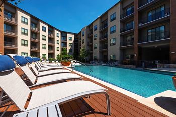 A pool area with sun loungers and apartment buildings in the background.