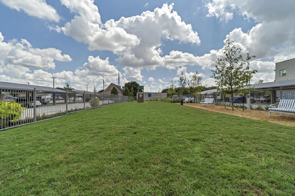 A large grassy field with a fence and a tree in the distance.