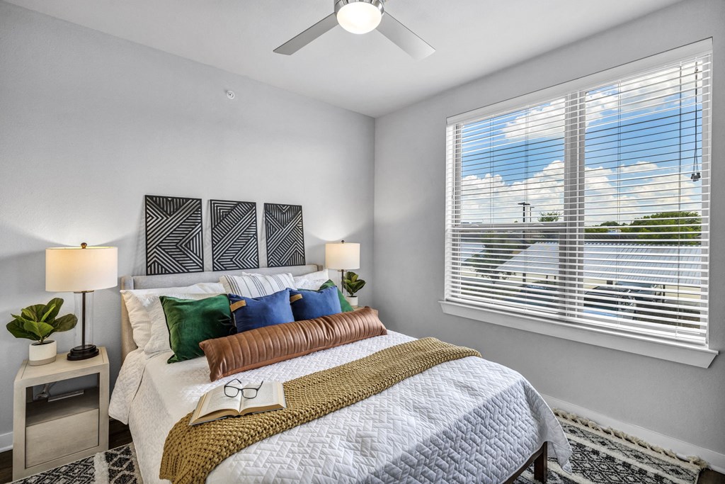 A bedroom with a bed, two lamps, and a window with blinds.