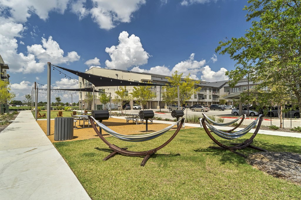 A park with a hammock and a building in the background.