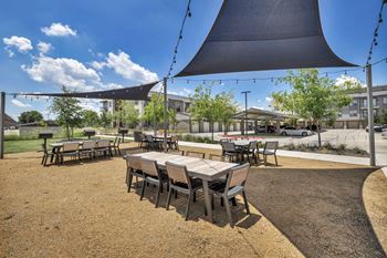 A large black shade sail is over a table set for dining.