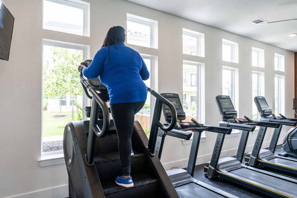 A woman in a blue top and black leggings is using a treadmill in a gym.