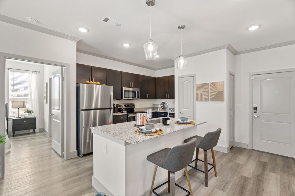 A modern kitchen with a white island and grey chairs.