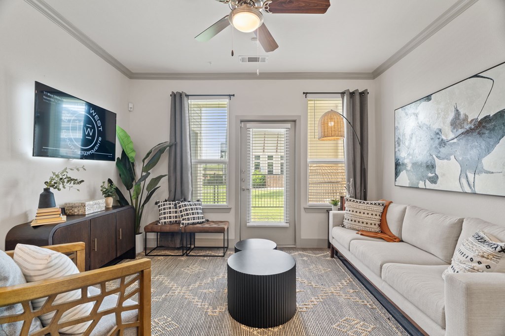 A living room with a white couch, a wooden chair, and a TV mounted on the wall.