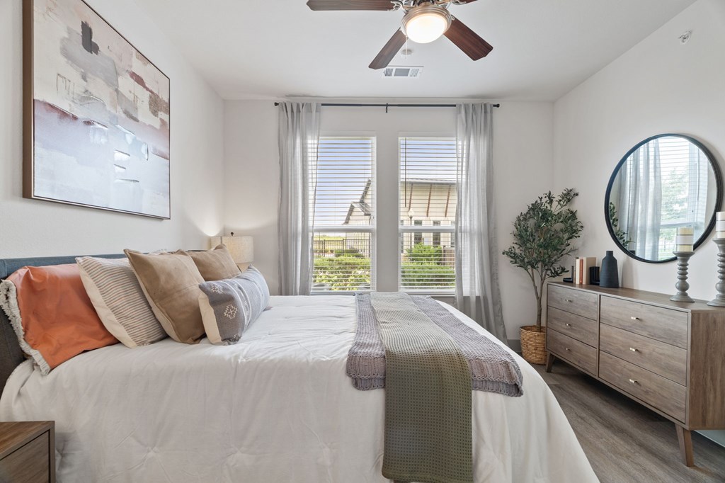A bedroom with a large bed, a ceiling fan, and a view of the backyard through the sliding glass doors.