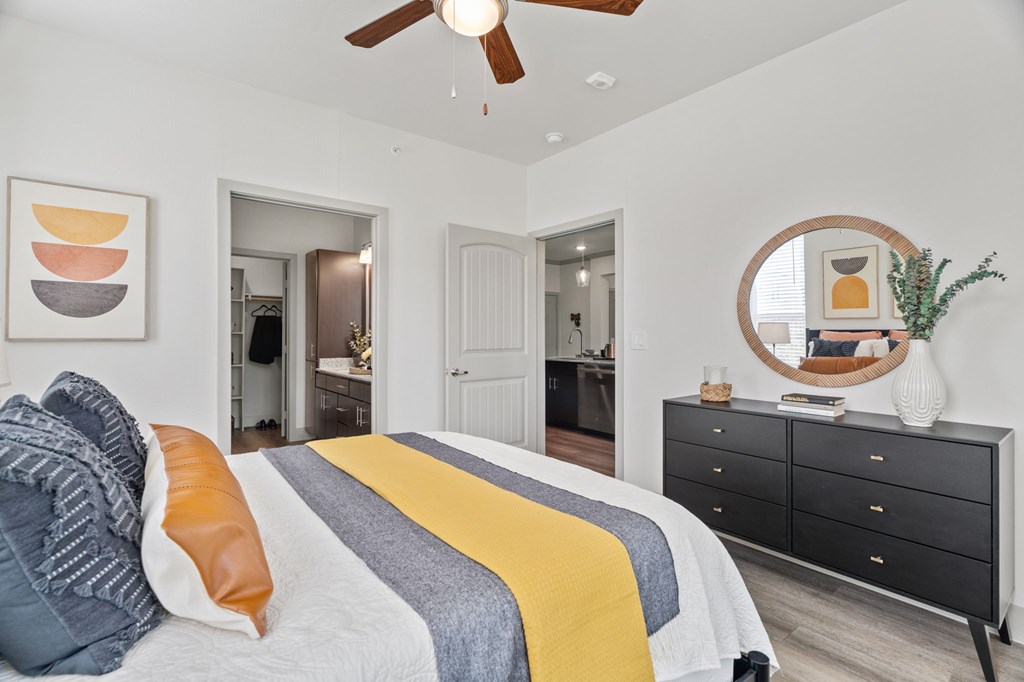 A bedroom with a bed, dresser, mirror, and a ceiling fan.