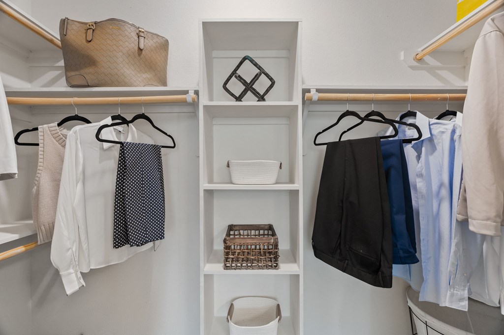 A white closet with clothes hanging and a purse on a shelf.