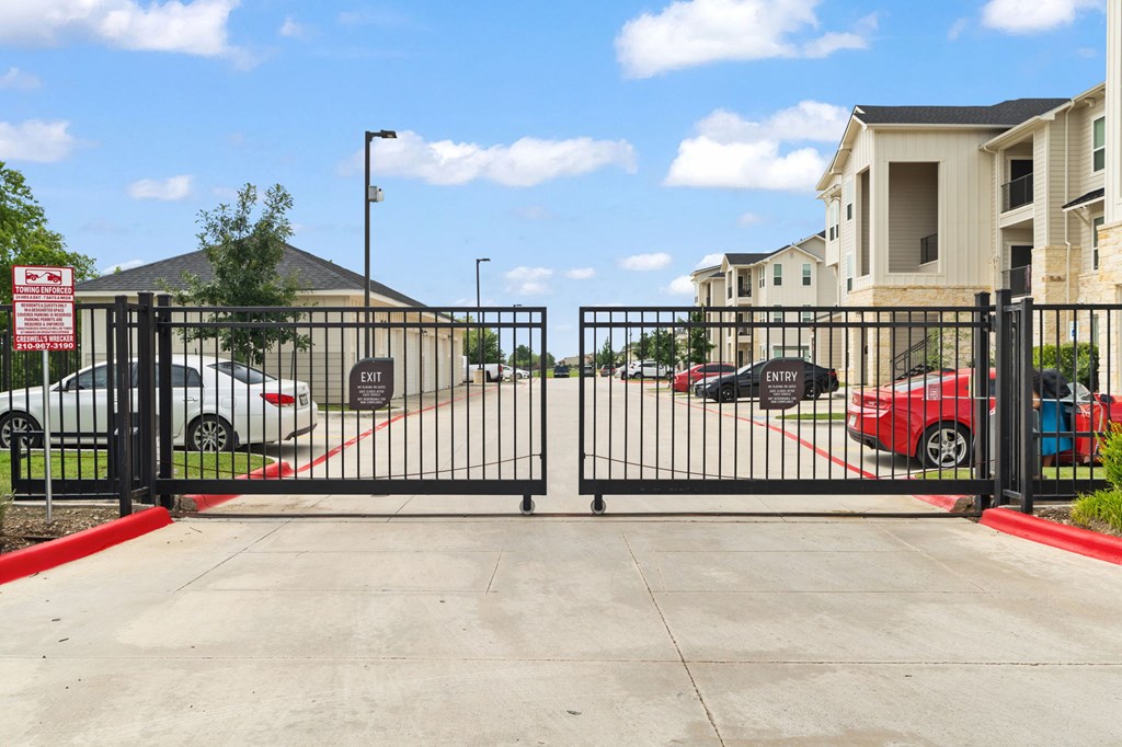 A black gate with a red sign on it blocks the entrance to a parking lot.
