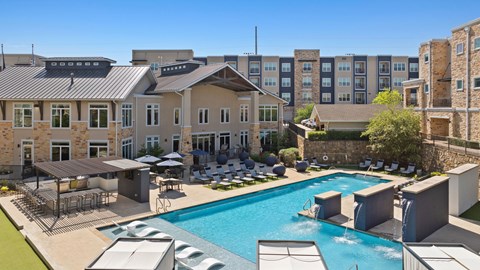 A large swimming pool surrounded by lounge chairs and umbrellas in front of a building.