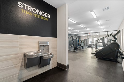 A gym with a wall that says "STRONGER THAN YESTERDAY" and a treadmill in the background.