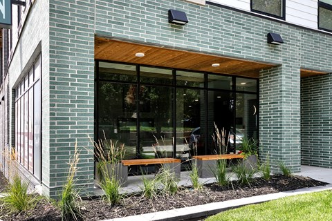 A modern building with a green brick facade and a wooden bench in front.