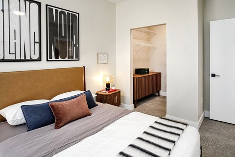 A bedroom with a bed, pillows, and a nightstand with a lamp.