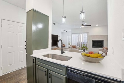 A kitchen with a sink and a bowl of fruit on the counter.