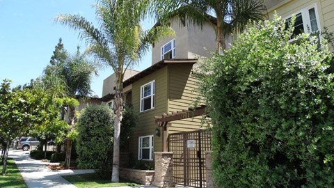 A house with a brown fence and a gate is surrounded by green trees.