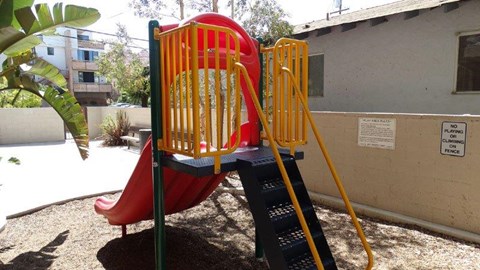 A red slide with a yellow ladder in a playground.