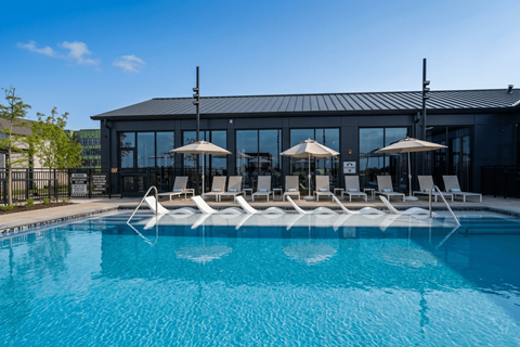 A pool with chairs and umbrellas in front of a building.