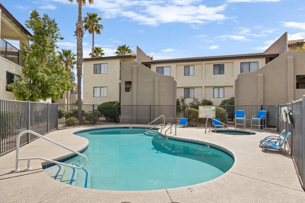 A swimming pool surrounded by a fence and chairs in front of a building.