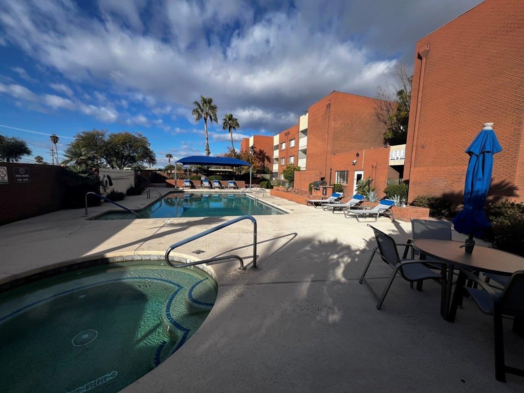 A pool with a blue umbrella and chairs around it.