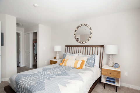A bedroom with a bed, two lamps, and a mirror on the wall.