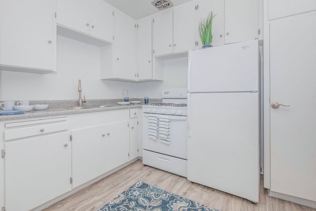A white kitchen with a refrigerator, sink, and cabinets.