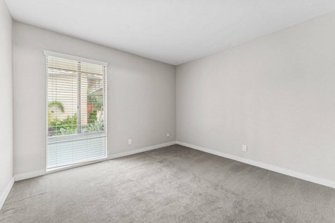 A room with a window and a view of a building and trees outside.