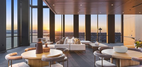 A modern living room with a large table and chairs overlooking a sunset.