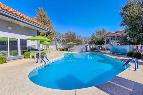 A swimming pool with a blue tinted water and a green umbrella.