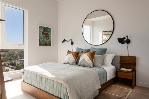 A bedroom with a bed, a round mirror, and a painting on the wall.