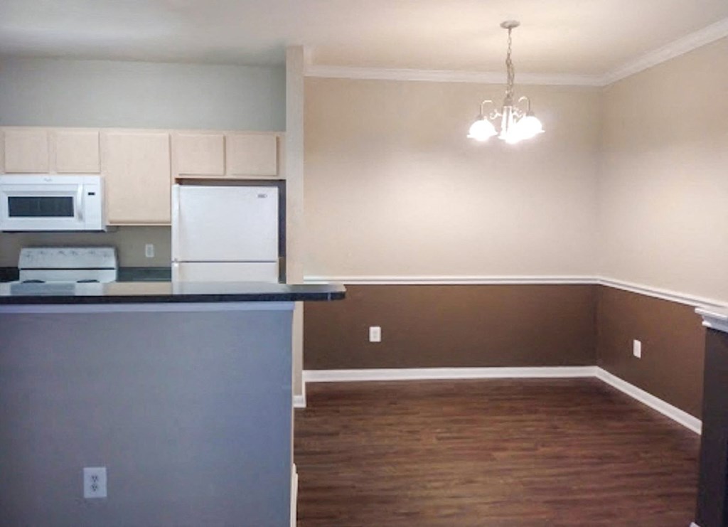an empty living room with a kitchen and a refrigerator